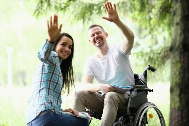 Woman and man in a wheelchair waving back happily