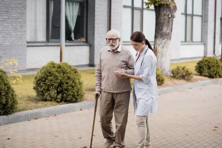 Elderly walking with cane assisted by caregiver