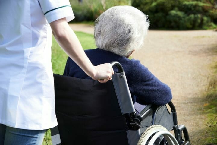 Nursing home staff pushing senior woman on wheelchair