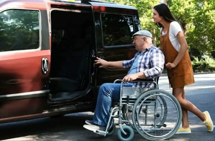 woman helping senior man in a wheelchair to get in the car