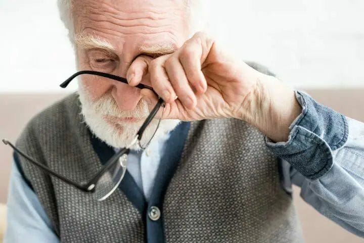 Sad senior man holding his eyeglasses