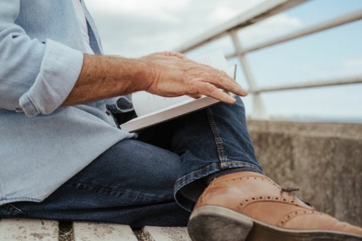 man reading a book while sitting on a bridge