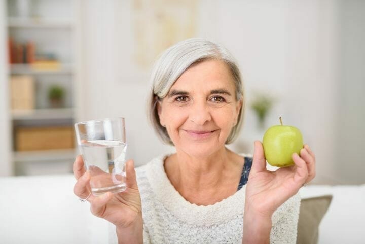 senior woman holding water and apple